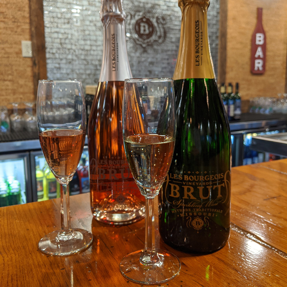 Bottles and flutes of Les Bourgeois Vineyards Brut and Brut Rose on a bar